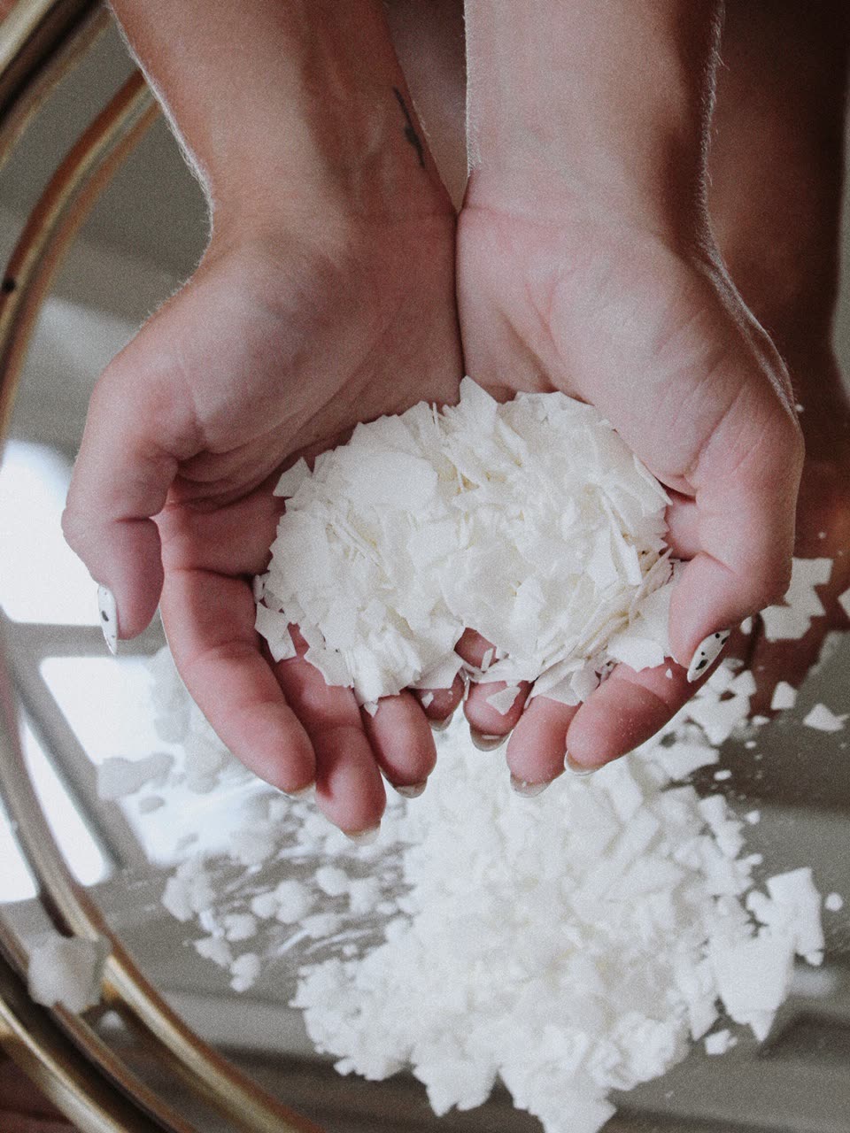 Two hands holding a pile of soy-coconut wax flakes.