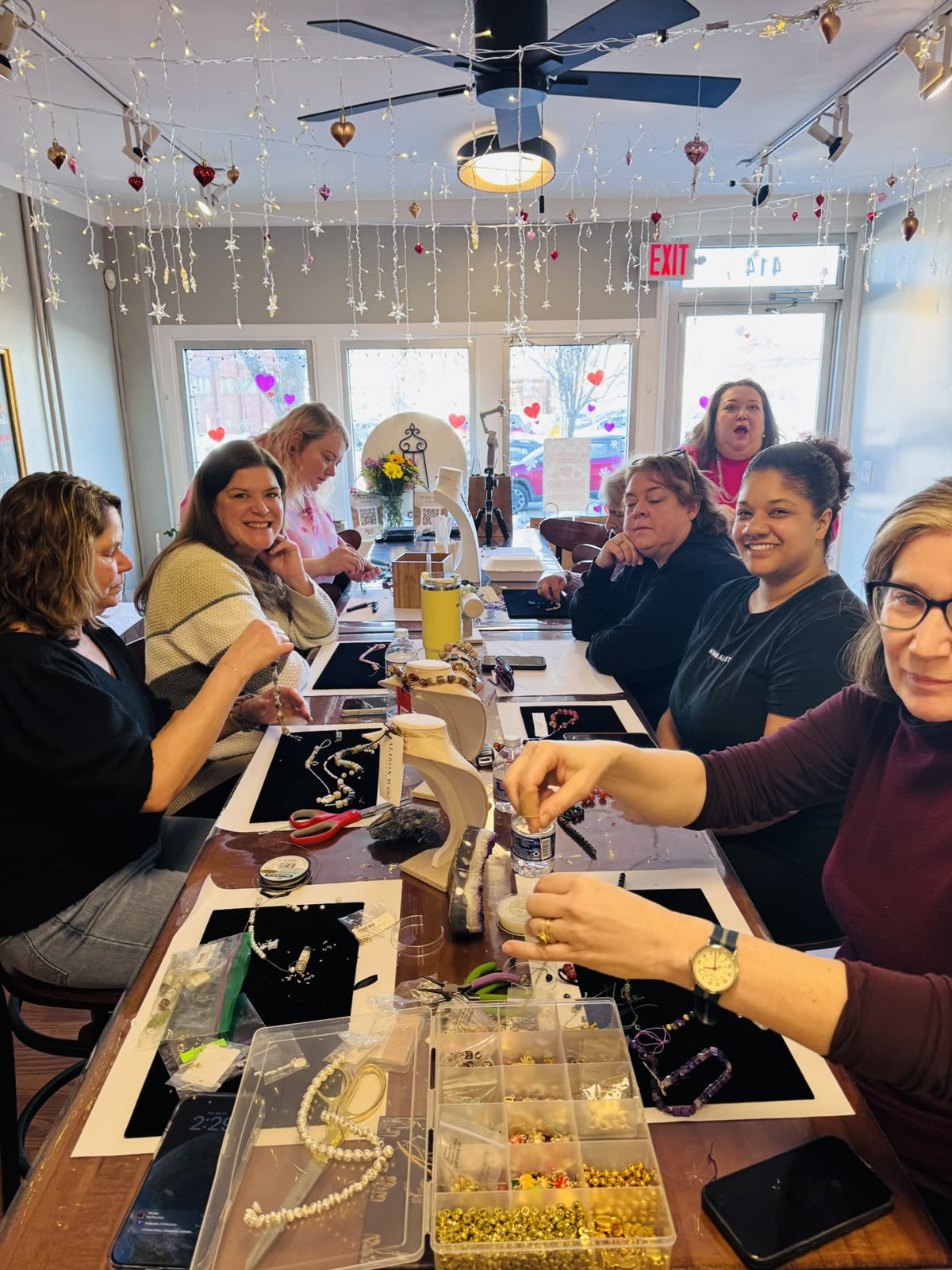 A full table of guests making candles under the studio's string lights.